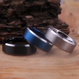 May include: Three tungsten carbide rings in black, blue, and silver. The rings have a beveled edge and a brushed finish.