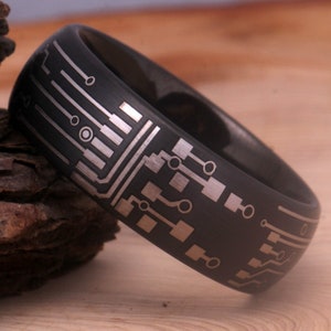 May include: A black tungsten carbide ring with a silver circuit board design. The ring has a brushed finish.