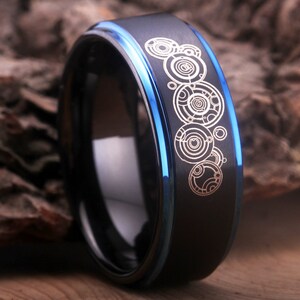 May include: A black tungsten carbide ring with a blue edge and a white design of the Doctor Who TARDIS console room.