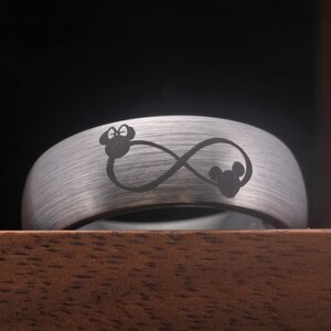 May include: A silver tungsten carbide ring with an infinity symbol and two Mickey Mouse heads engraved on it.