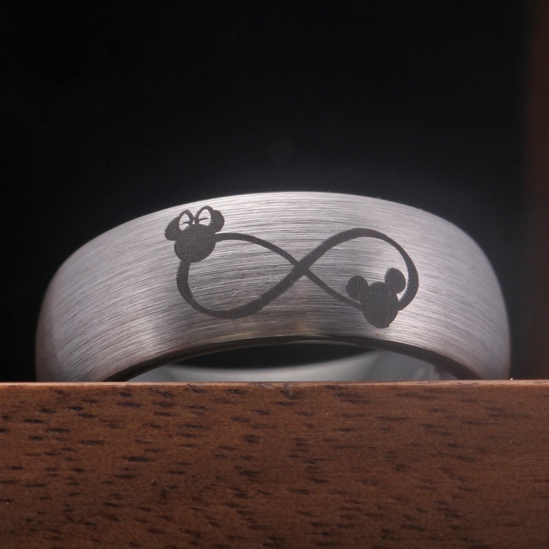 May include: A silver tungsten carbide ring with an infinity symbol and two Mickey Mouse heads engraved on it.
