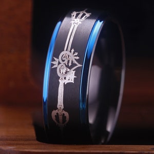 May include: A black and blue ring with a silver engraved design of a keyblade and heart. The ring is made of tungsten carbide.