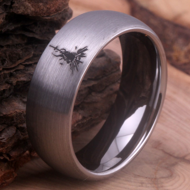 Op de afbeelding: Een geborstelde zilveren ring van wolframcarbide met een zwarte binnenband en een lasergegraveerd ontwerp aan de bovenkant.