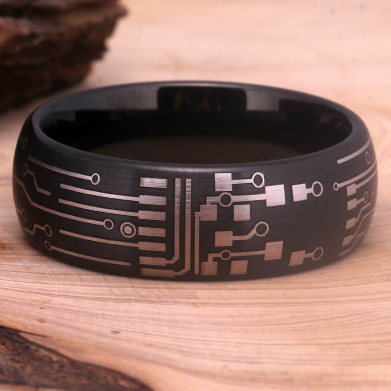 May include: A black tungsten carbide ring with a brushed finish and a silver circuit board design.