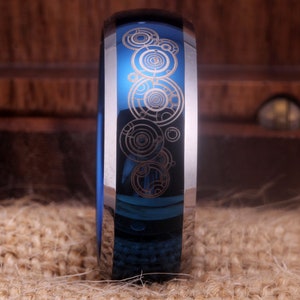 May include: A blue and silver ring with a design of a series of concentric circles etched into the band.