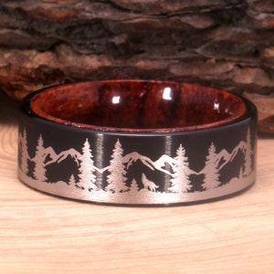 Peut inclure: Une bague noire et brune avec un incrustation argentée représentant un loup hurlant à la lune dans une scène de forêt de montagne.