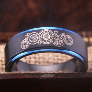 May include: A black tungsten carbide ring with a blue inlay and a laser-etched design of the TARDIS console room from Doctor Who.