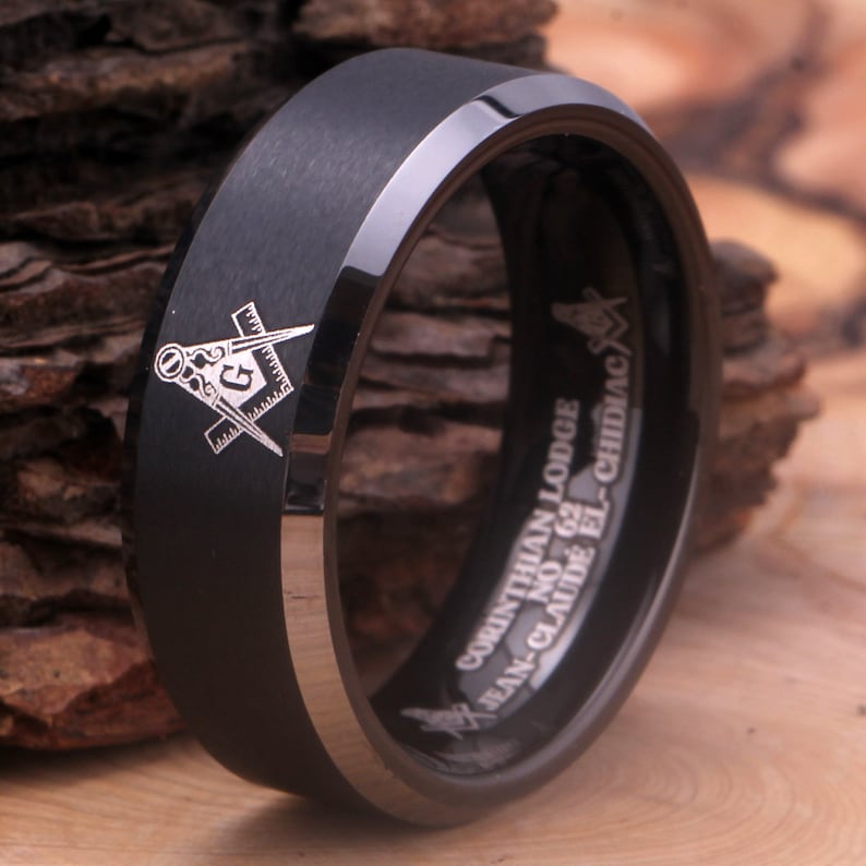 May include: A black tungsten carbide ring with a silver Masonic symbol engraved on the front and the inscription "CORINTHIAN LODGE NO. 62 JEAN-CLAUDE EL-CHIDIAC" engraved on the inside.