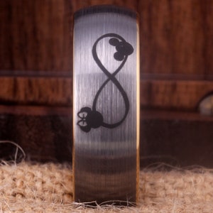 May include: A silver wedding band with a brushed finish and an infinity symbol engraved on the top. The infinity symbol is intertwined with two small Mickey Mouse heads.