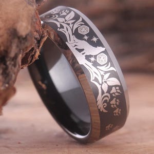 May include: A black tungsten carbide ring with a silver wolf, paw prints, and floral design engraved on the band.