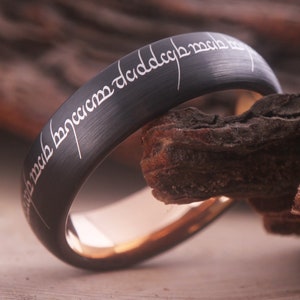 Op de afbeelding: Een zwarte ring van wolfraamcarbide met een binnenband van roségoud. De ring is gegraveerd met de inscriptie "Een Ring om ze te regeren, Een Ring om ze te vinden, Een Ring om ze allen te brengen en in de duisternis te binden."