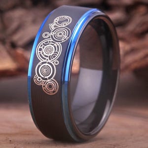 Könnte beinhalten: Ein schwarzer Ring aus Wolframcarbid mit einer blauen Kante und einem silbernen Design des Doctor Who TARDIS-Symbols.