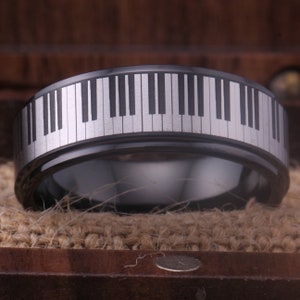 May include: A black tungsten carbide ring with a silver piano keyboard design engraved around the band.