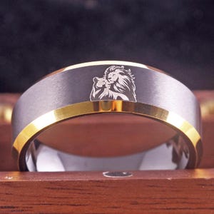 May include: A silver and gold ring with a lion and lioness design. The ring is engraved with a couple of lions embracing.