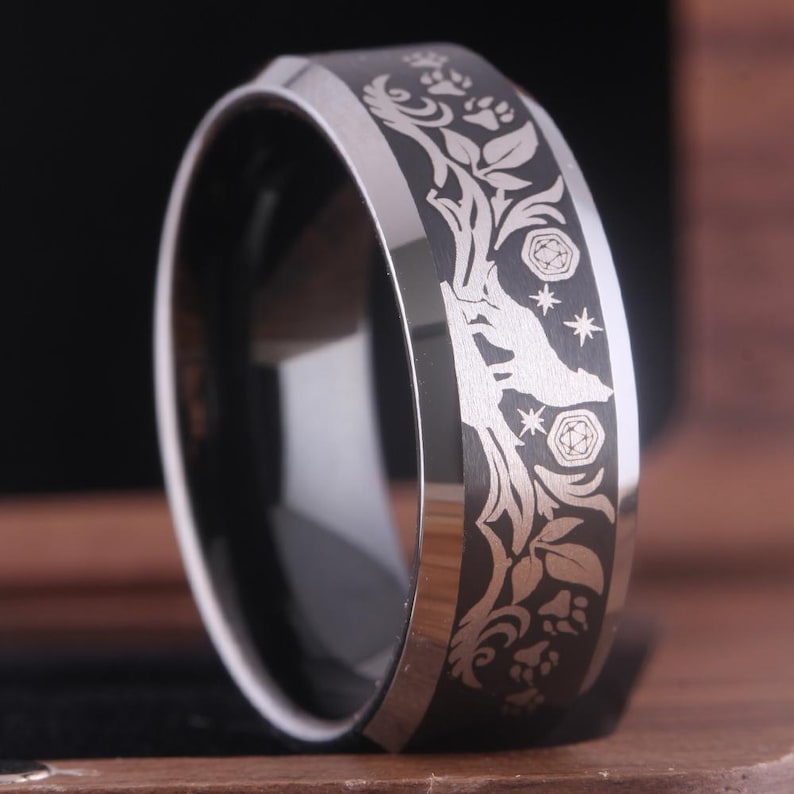 May include: A black tungsten carbide ring with a silver wolf, paw prints, and floral design engraved on the band.