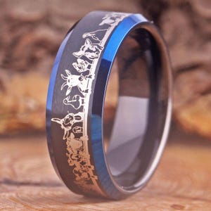 Puede incluir: Un anillo de carburo de tungsteno negro y azul con un diseño grabado en plata de una línea de cabras.