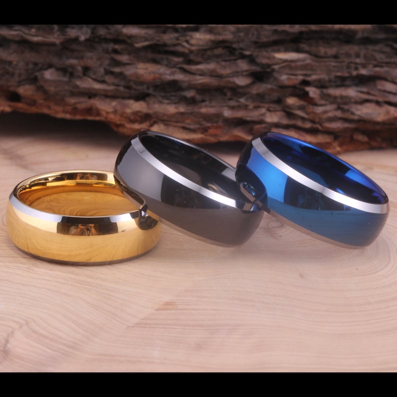 May include: Three men's wedding bands in different colors. The bands are made of tungsten carbide and have a beveled edge. The bands are gold, black, and blue.