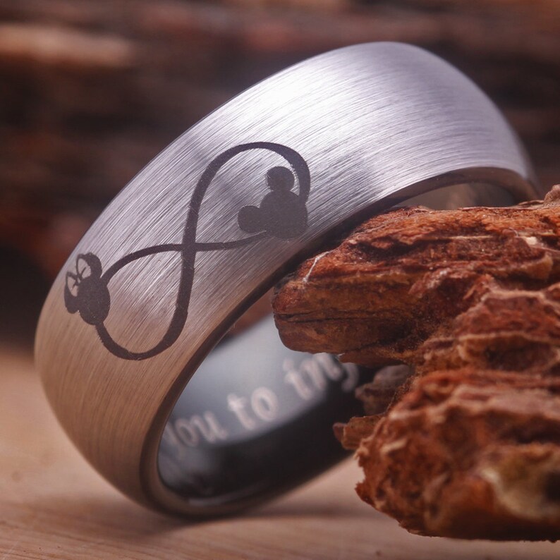 May include: A silver tungsten carbide ring with an infinity symbol and two Mickey Mouse heads engraved on it. The ring is engraved with the words "You to infinity".