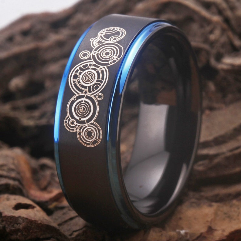 May include: A black tungsten carbide ring with a blue edge and a silver design of the TARDIS console room on the top.