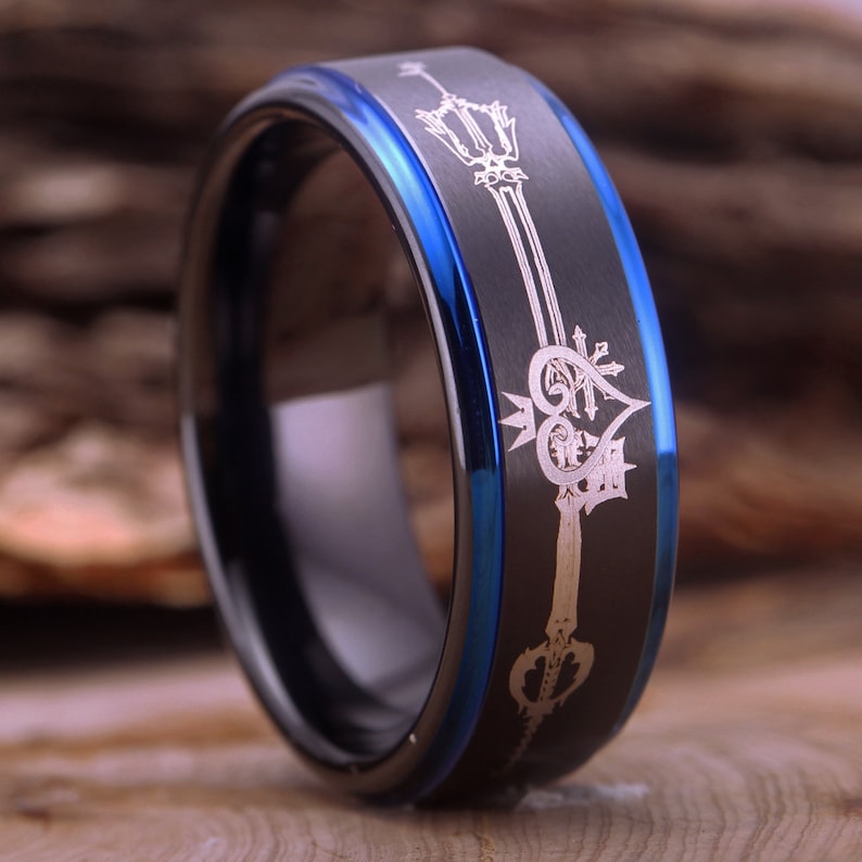 May include: A black and blue tungsten carbide ring with a silver engraved design of a keyblade and heart.