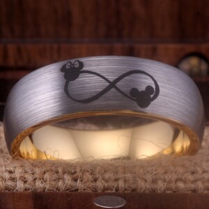 May include: A silver and gold wedding band with an infinity symbol and two Mickey Mouse heads engraved on it.