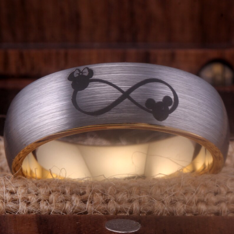 May include: A silver and gold wedding band with an infinity symbol and two Mickey Mouse heads engraved on it.