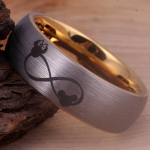 May include: A silver tungsten carbide ring with a gold band and an infinity symbol with Mickey Mouse heads engraved on it.