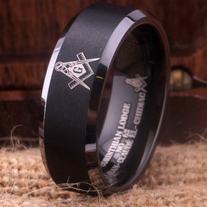 May include: Black tungsten carbide ring with a silver Masonic symbol and the inscription "CORINTHIAN LODGE NO. 62  JEAN-CLAUDE EL-CHIDIAC"