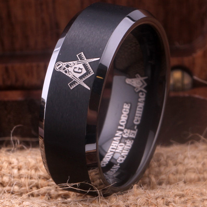 May include: Black tungsten carbide ring with a silver Masonic symbol and the inscription "CORINTHIAN LODGE NO. 62  JEAN-CLAUDE EL-CHIDIAC"