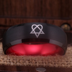 May include: Black tungsten carbide ring with a red interior and a silver engraved symbol of a heart with a star inside.