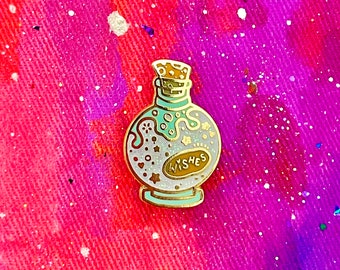 May include: A gold-colored enamel pin shaped like a bottle with a cork stopper. The bottle is filled with white glitter and has the word "Wishes" written on it.