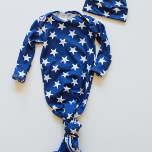 May include: A blue and white star patterned knotted gown and matching hat for a newborn baby. The gown has long sleeves and a knotted bottom. The hat has a knot on top.