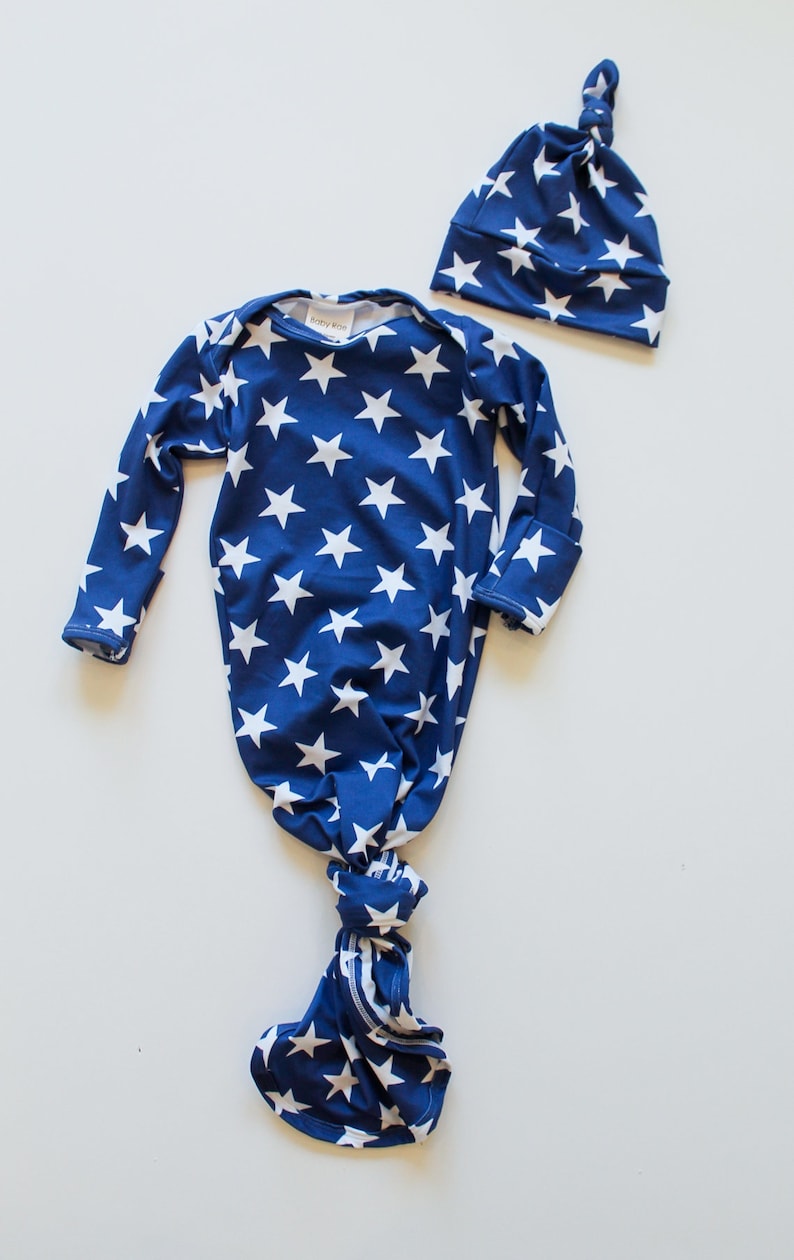 May include: A blue and white star patterned knotted gown and matching hat for a newborn baby. The gown has long sleeves and a knotted bottom. The hat has a knot on top.