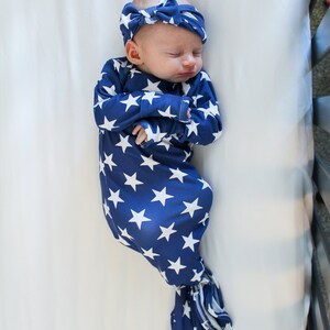 May include: A baby wearing a blue and white star patterned swaddle with a matching headband. The baby is sleeping in a white crib.