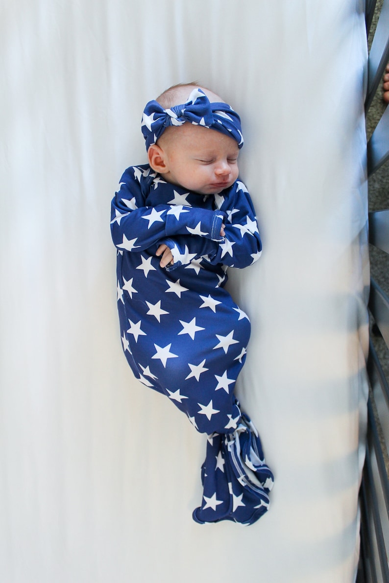 May include: A baby wearing a blue and white star patterned swaddle with a matching headband. The baby is sleeping in a white crib.