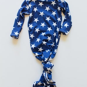 May include: A blue and white knotted baby gown with a star pattern. The gown has long sleeves and a knotted bottom. The label says "Baby Rae".