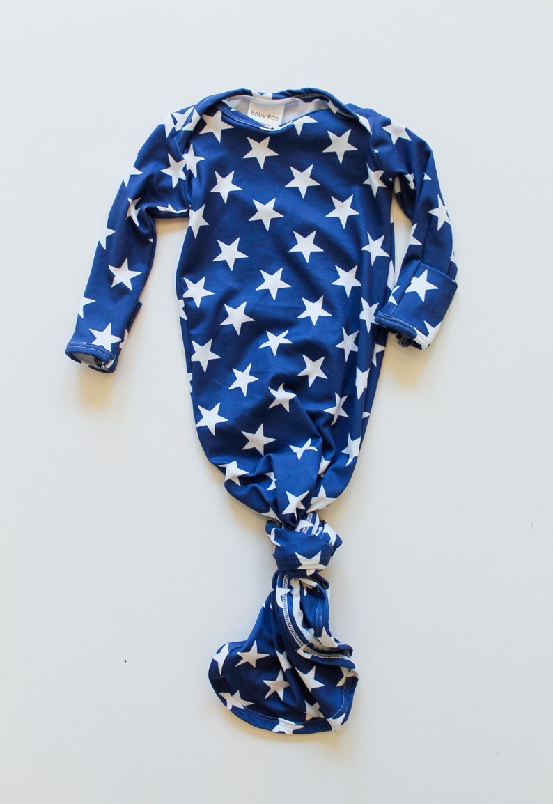 May include: A blue and white knotted baby gown with a star pattern. The gown has long sleeves and a knotted bottom. The label says "Baby Rae".