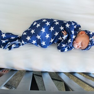 May include: A newborn baby sleeping in a blue and white star patterned swaddle. The baby is wearing a matching headband and has a pacifier in their mouth.