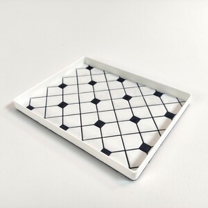 May include: A white rectangular tray with a black and white geometric pattern. The pattern is made up of small squares and diamonds.
