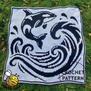 May include: A crocheted blanket with a black and white orca whale design and ocean waves. The blanket has a light grey background and a black border. The words "CROCHET PATTERN" are visible on the blanket.