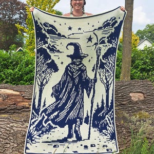 May include: A cream-colored crocheted blanket featuring a dark blue wizard design. The wizard is depicted with a staff, surrounded by trees and stars. The blanket has a dark blue border.