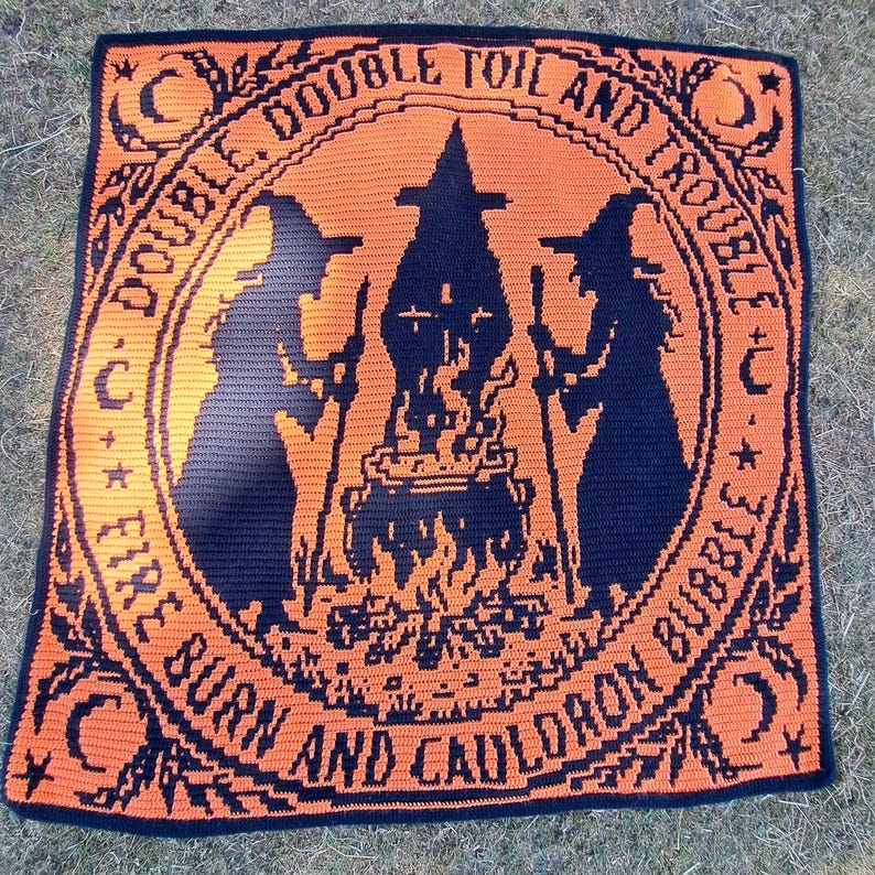 May include: A square crochet blanket featuring a black and orange design of two witches standing over a bubbling cauldron. The text "DOUBLE, DOUBLE TOIL AND TROUBLE, FIRE BURN AND CAULDRON BUBBLE" is written in a circular border with moon and star motifs.