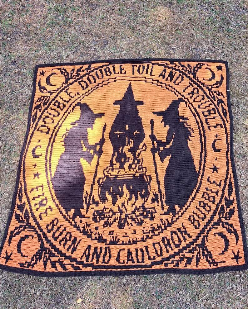 May include: A square crochet blanket featuring a black and orange design. The center depicts two silhouettes of witches standing by a bubbling cauldron over a fire. The text reads DOUBLE, DOUBLE TOIL AND TROUBLE, FIRE BURN AND CAULDRON BUBBLE.