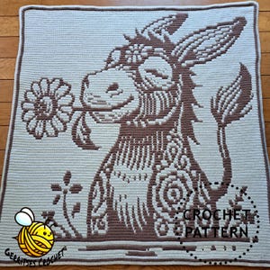 May include: Crochet pattern for a donkey holding a flower. The donkey is brown and the flower is white. The pattern is on a white background with the text "CROCHET PATTERN" in the bottom right corner.