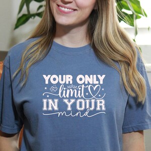 Könnte beinhalten: Ein blaues T-Shirt mit dem Text "YOUR ONLY limit IN YOUR mind" in weißer Schrift. Das Shirt hat kurze Ärmel und einen Rundhalsausschnitt. Die Person auf dem Bild trägt eine blaue Jeans.