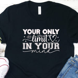 Könnte beinhalten: Schwarzes T-Shirt mit dem weißen Text "YOUR ONLY LIMIT IS IN YOUR MIND". Das Shirt wird mit Jeansshorts, weißen Turnschuhen und einer kleinen Pflanze kombiniert. Das T-Shirt ist ein Freizeitkleidungsstück.