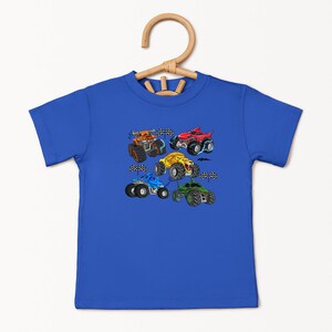 Puede incluir: Una camiseta azul real con un gr&aacute;fico colorido de seis monster trucks de dibujos animados. Los camiones son de varios colores, incluyendo naranja, rojo, amarillo, azul y verde, con neum&aacute;ticos negros y banderas a cuadros.