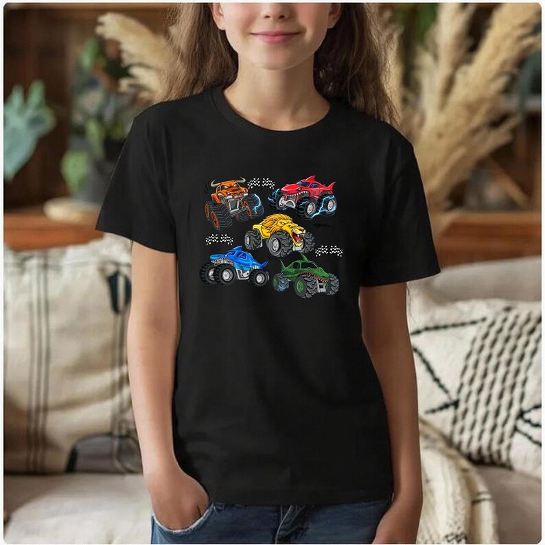 Puede incluir: Camiseta negra con dise&ntilde;os de monster trucks coloridos. Los camiones son de varios colores, incluyendo naranja, rojo, amarillo, azul y verde, cada uno con detalles &uacute;nicos. El dise&ntilde;o est&aacute; centrado en la camiseta, haci&eacute;ndola divertida.