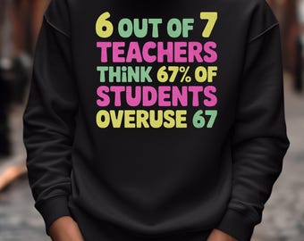 Può includere: Felpa nera con la scritta "6 OUT OF 7 TEACHERS THINK 67% OF STUDENTS OVERUSE 67" in giallo, rosa e verde. Un capo d'abbigliamento casual.