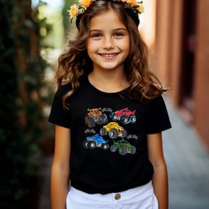 Puede incluir: Camiseta negra con dise&ntilde;os de monster trucks coloridos. Los camiones son de varios colores, incluyendo naranja, rojo, amarillo, azul y verde. La camiseta la lleva una persona con una corona de flores.
